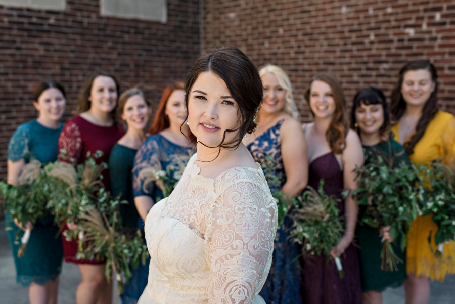 A bride stands in front of her bridesmaids as the wind blows her hair.
